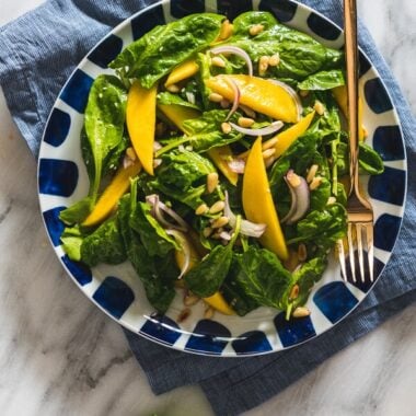 The spinach salad is served with a refreshing sweet and sour vinaigrette with sweet mango slices and toasted pine nuts. It takes no time to put together and adds a delicious green to your main dish!