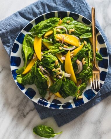 The spinach salad is served with a refreshing sweet and sour vinaigrette with sweet mango slices and toasted pine nuts. It takes no time to put together and adds a delicious green to your main dish!