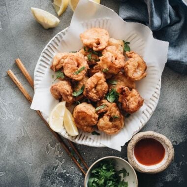 Fried shrimp served in plate with parchment paper with chopped cilantro and sauce on the side