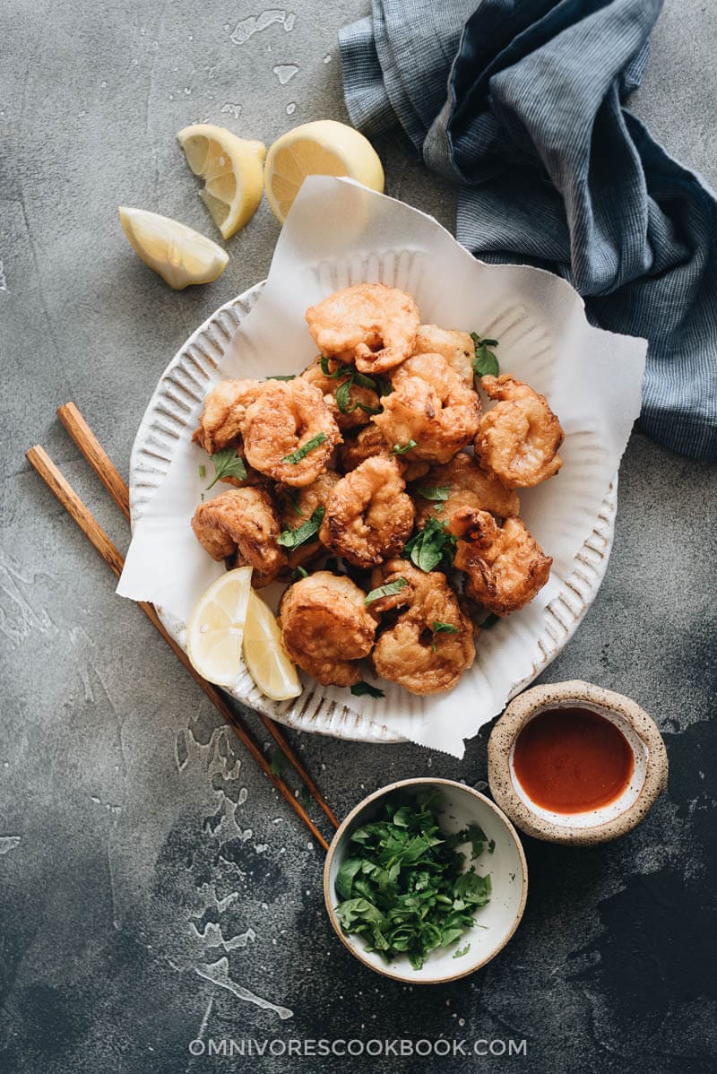 3-Ingredient Fried Shrimp is the easiest fried shrimp recipe that generates the best results. The juicy shrimp are wrapped in a light, crispy, and fluffy crust that is similar to tempura. So good! #seafood #recipes #shrimp Fried shrimp served in plate with parchment paper with chopped cilantro and sauce on the side