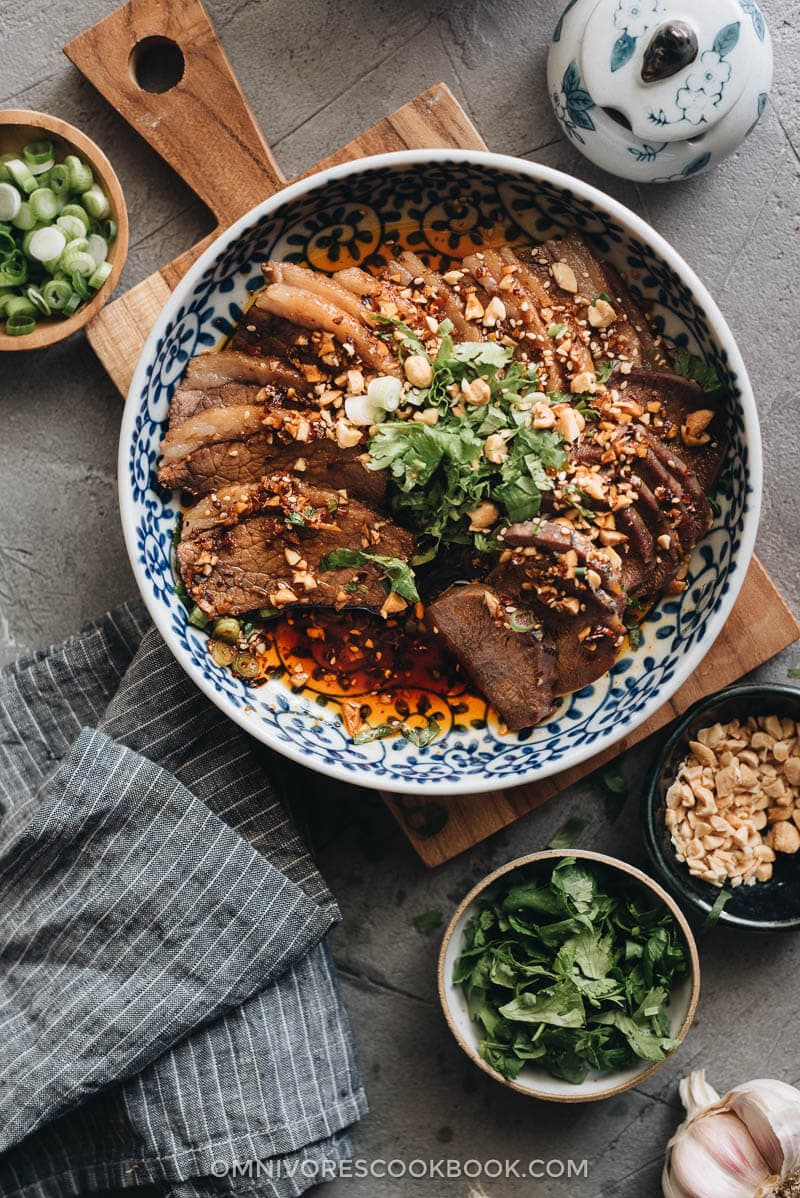 This Fu Qi Fei Pian (Sichuan Sliced Beef in Chili Sauce) recipe gives you the real-deal Sichuan experience. The tender beef slices are served in a rich, spicy hot sauce and topped with peanut flakes and cilantro. #glutenfree #beef #instantpot #chinese #recipes A plate of Fu Qi Fei Pian with aromatics and peanuts on the side