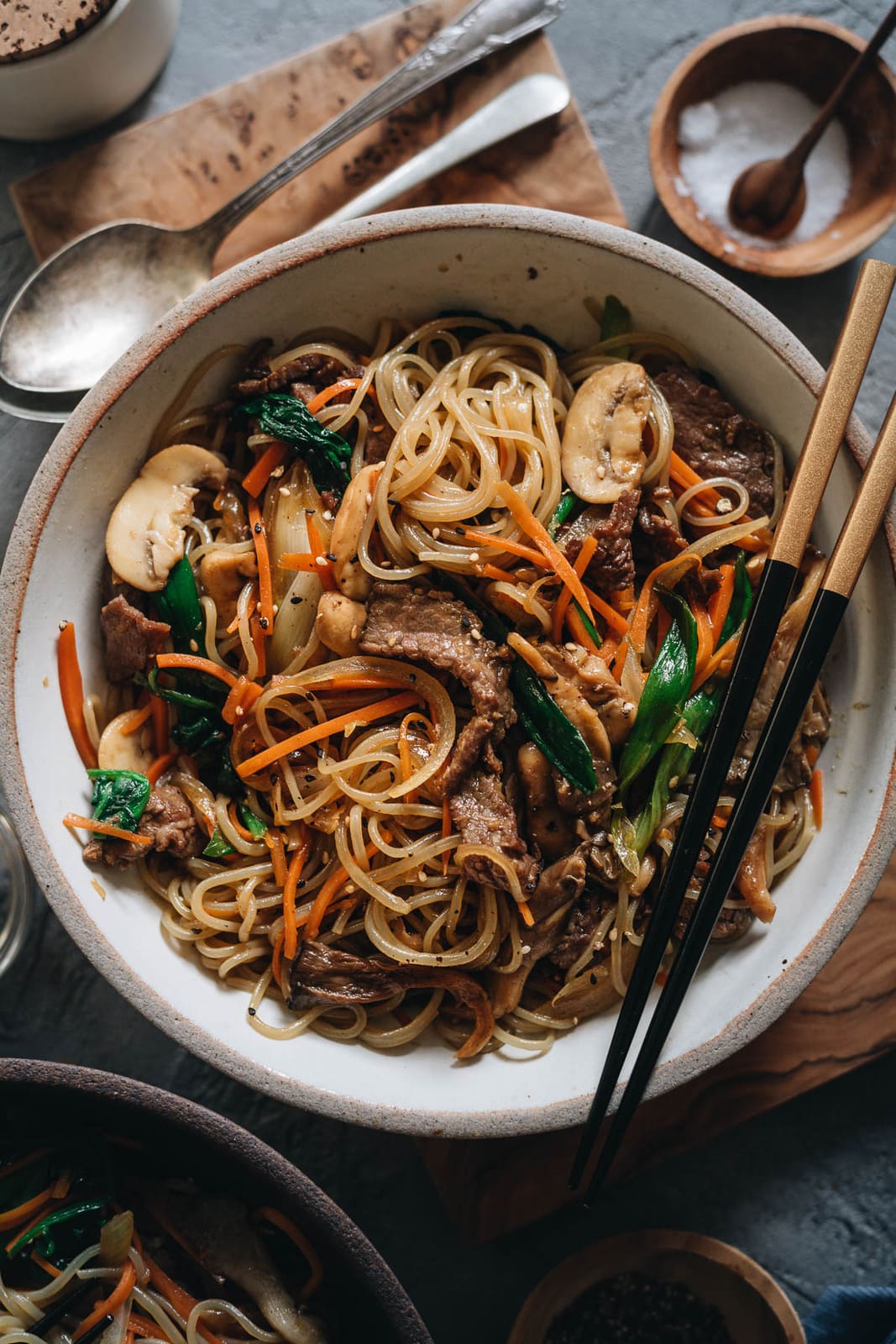 Japchae (Korean Sweet Potato Noodles) | Make japchae at home for a comforting, delicious, and nutritionally balanced weekday dinner. The tender sweet potato noodles are tossed with charred beef and crispy veggies in a sweet savory sauce. This easy recipe uses shortcuts to make the cooking process faster than the traditional recipe. {Gluten Free adaptable, vegan adaptable} Japchae in a bowl
