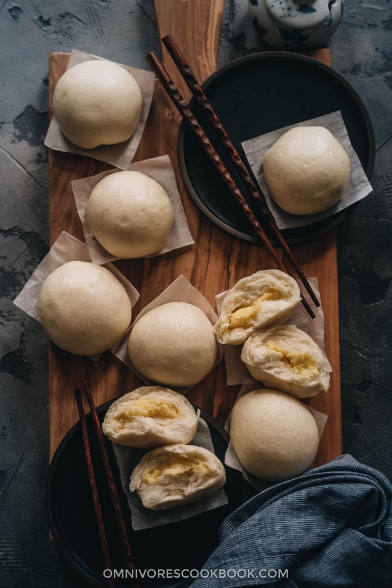 Chinese Steamed Custard Buns (nai wong bao, 奶黄包) | A dim sum classic, these buns are perfect for holiday gatherings and parties as well. Made with a yeast dough and steamed, the buns have a super soft and spongy texture with a smooth surface. The custard filling is creamy, fragrant, and sweet. The recipe includes detailed step-by-step pictures to help you recreate the restaurant-style custard buns in your own kitchen. Dim sum custard buns on a cutting board