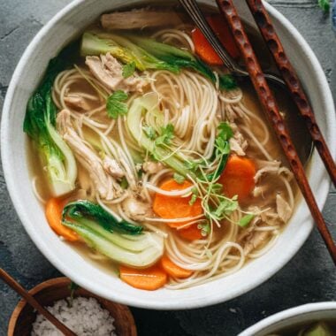 Bowl of noodle soup with shredded chicken, carrot and baby bok choy
