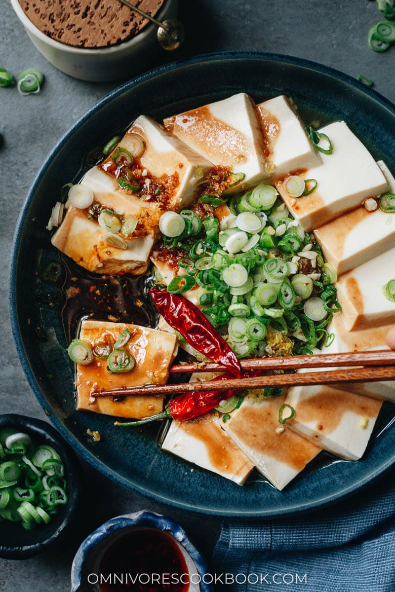 Chopsticks holding a piece of soft tofu with sauce