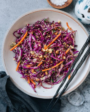 Crisp Chinese coleslaw with purple cabbage, carrots, peanuts, and cilantro in a ceramic bowl with chopsticks.