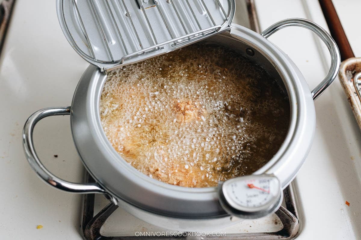 Chicken wings frying in hot oil inside a deep pot, with bubbling oil and a thermometer clipped to the side.