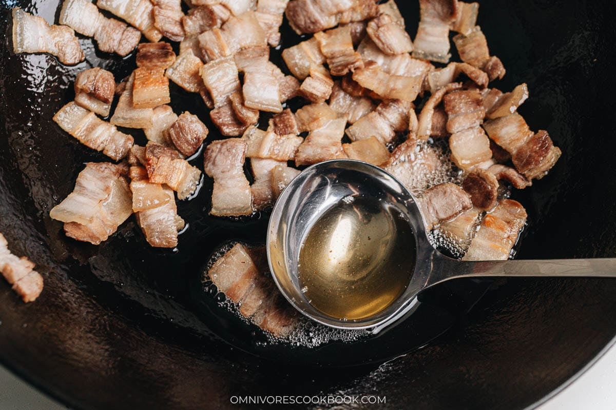 A ladle scooping out excess rendered fat from the wok.