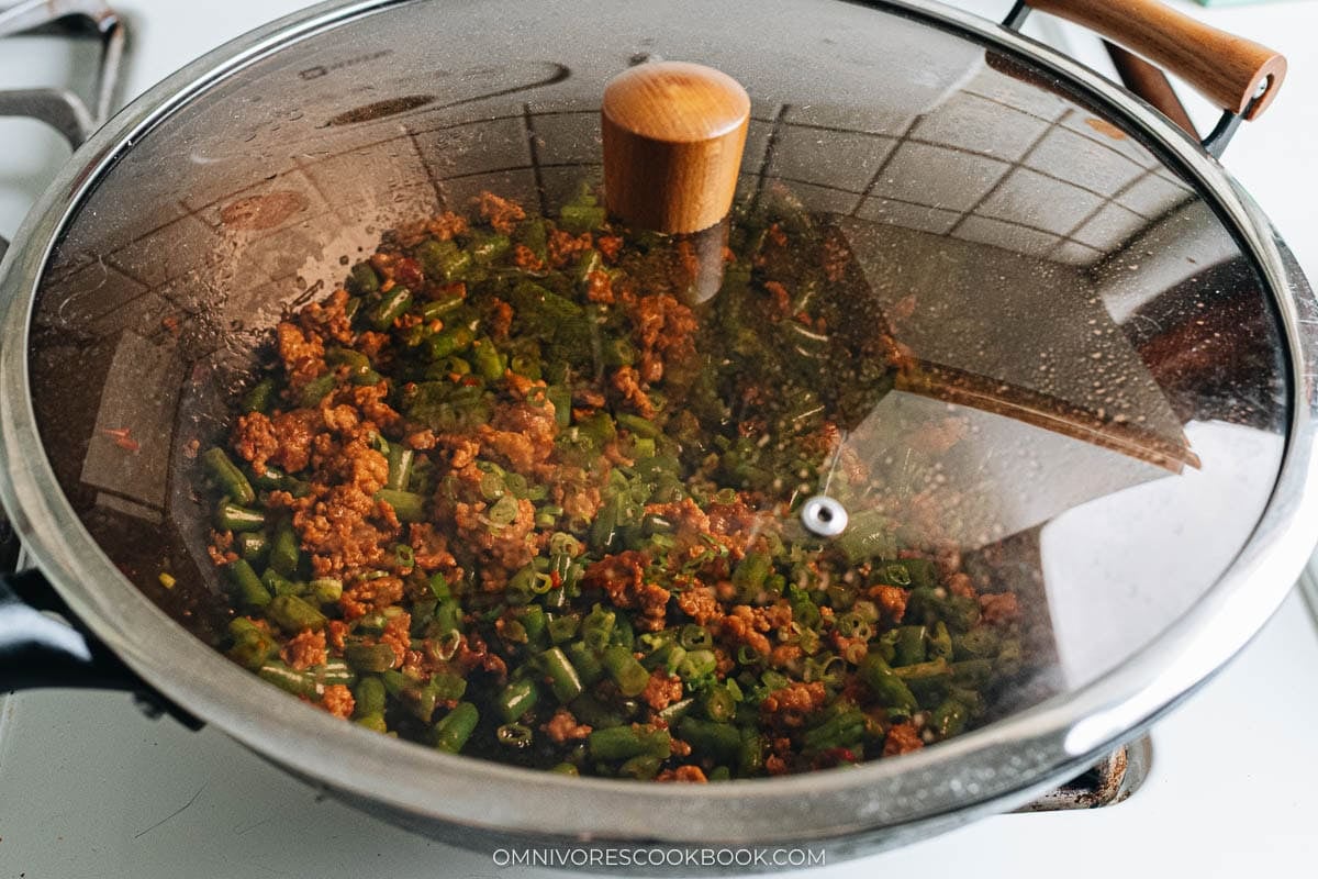 Green beans and ground pork simmering in a covered wok