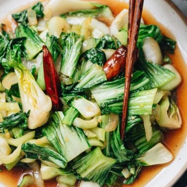 Chopsticks lifting bok choy coated in oyster sauce