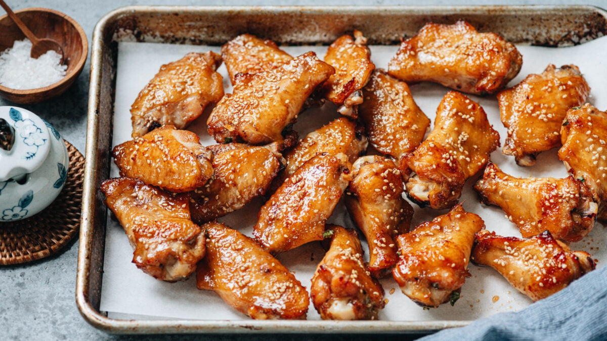 Chinese Baked crispy chicken wings on a baking sheet with sesame seeds.